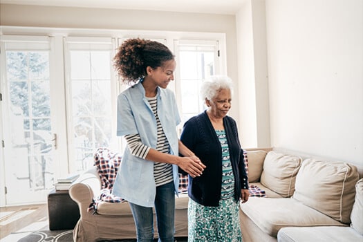 Homecare worker assists elderly woman to couch